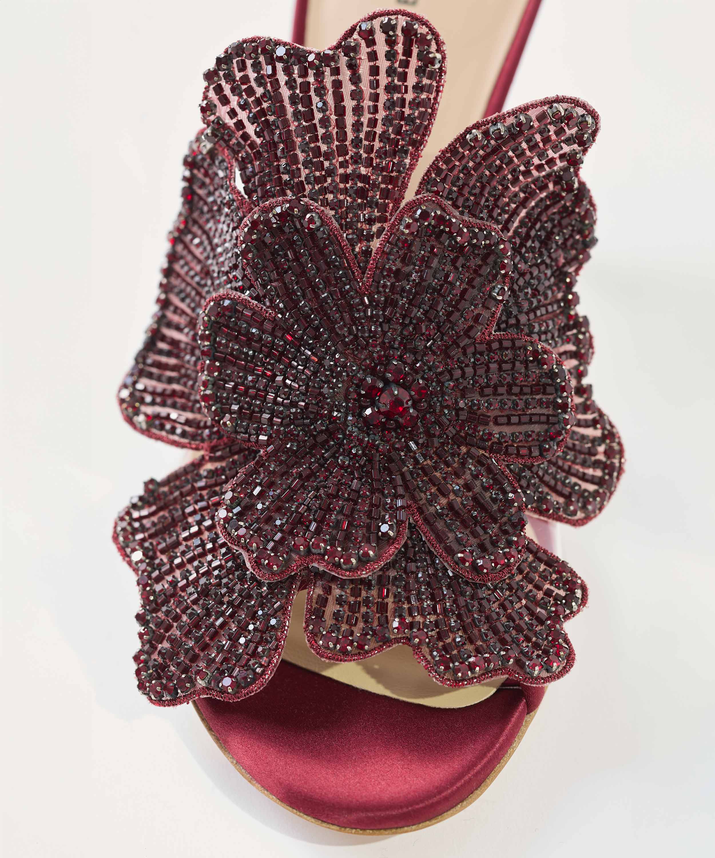 Red heeled mule with a large floral embellishment on a white background