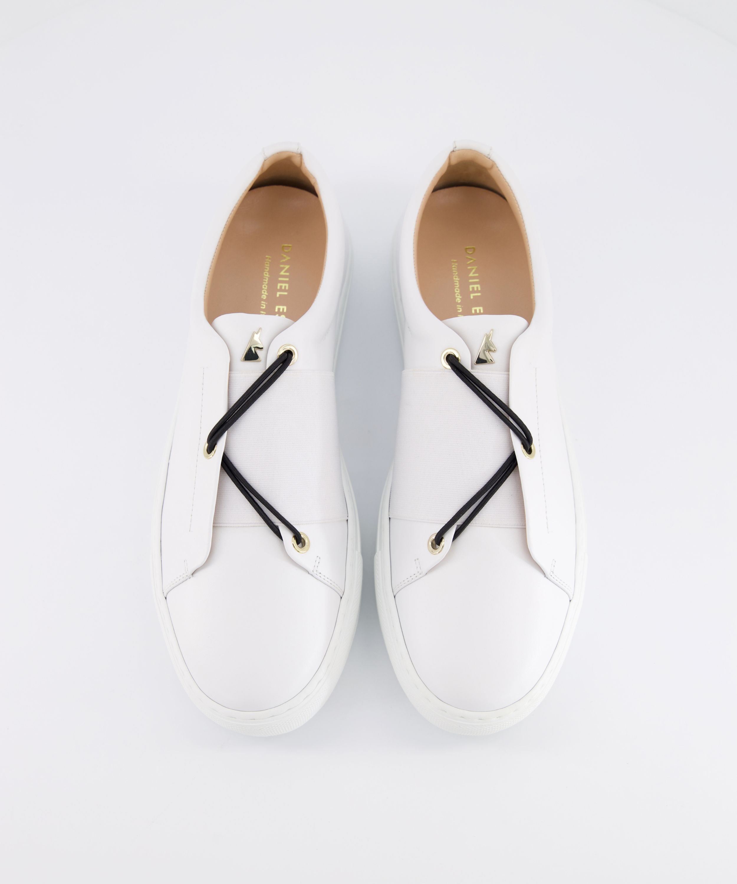 Top view of a pair of white leather Toi&Moi men sneakers with black elastic laces, gold eyelets, and a gold horse-head logo charm on the tongue.
