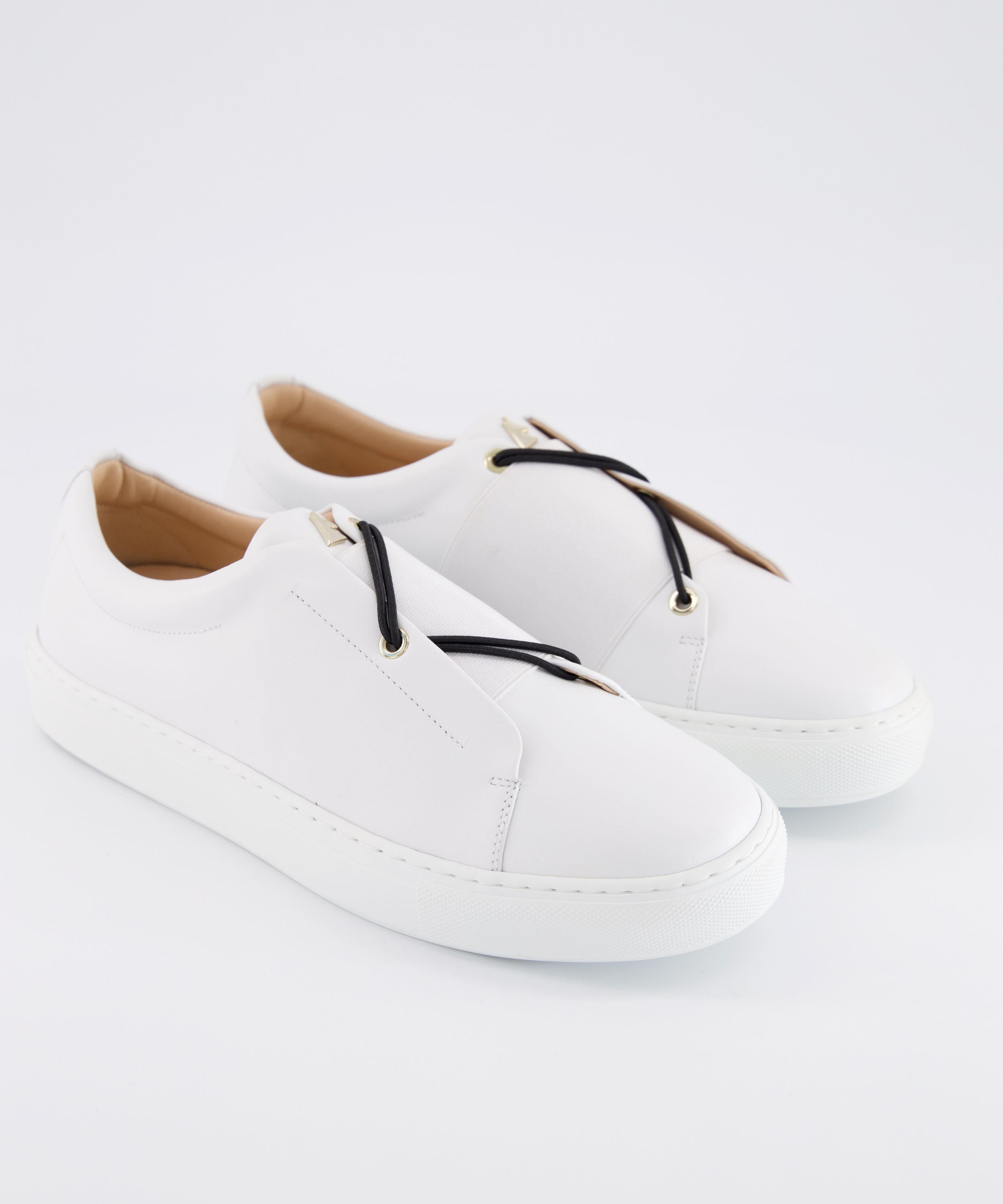 Three-quarter view of a pair of white leather Toi&Moi men sneakers with black elastic laces, gold eyelets, and a gold logo charm on the tongue.