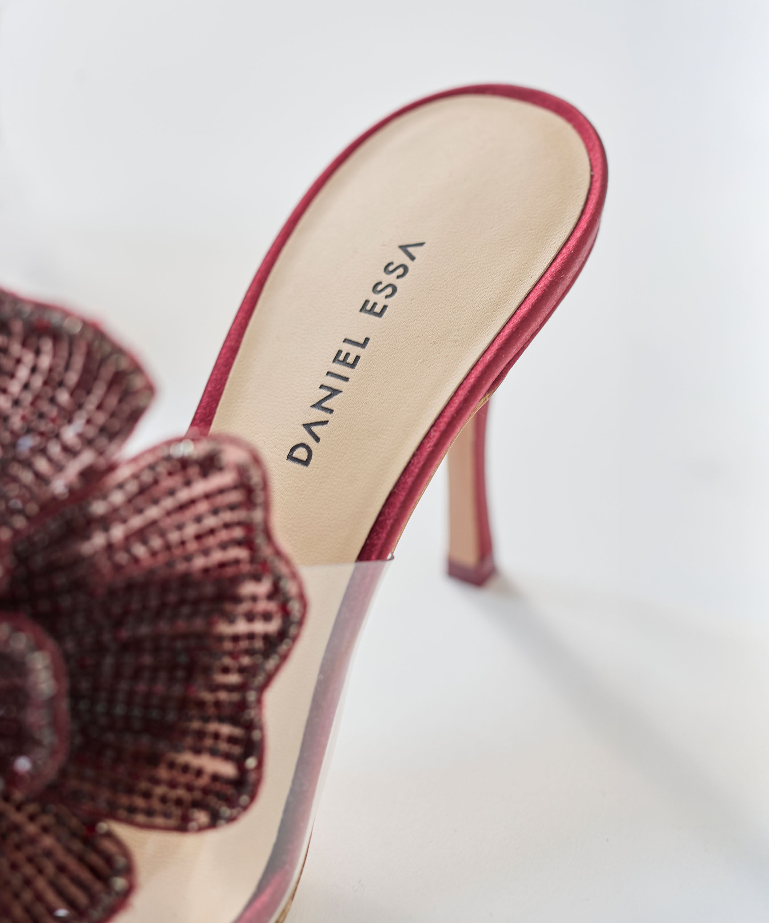 High-heeled red shoe with floral design and 'Daniel Essa' branding on a light background
